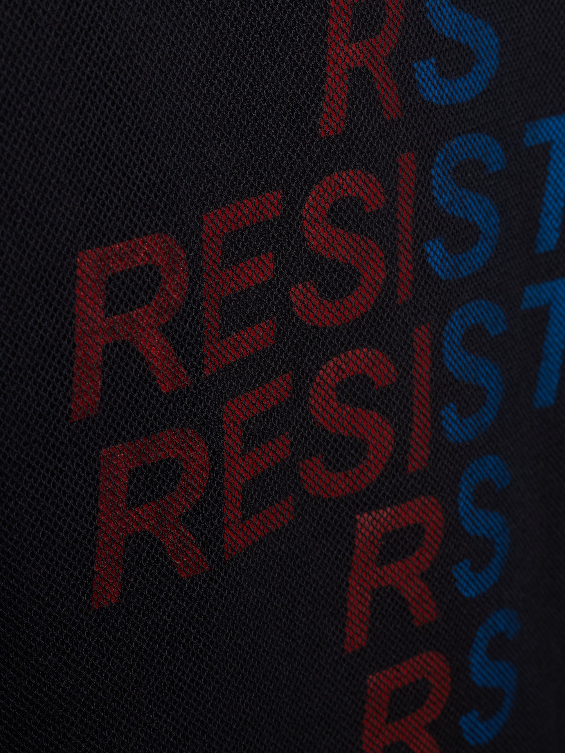 Close-up of a black textured fabric with large repeating 'RESIST' lettering in red and blue.