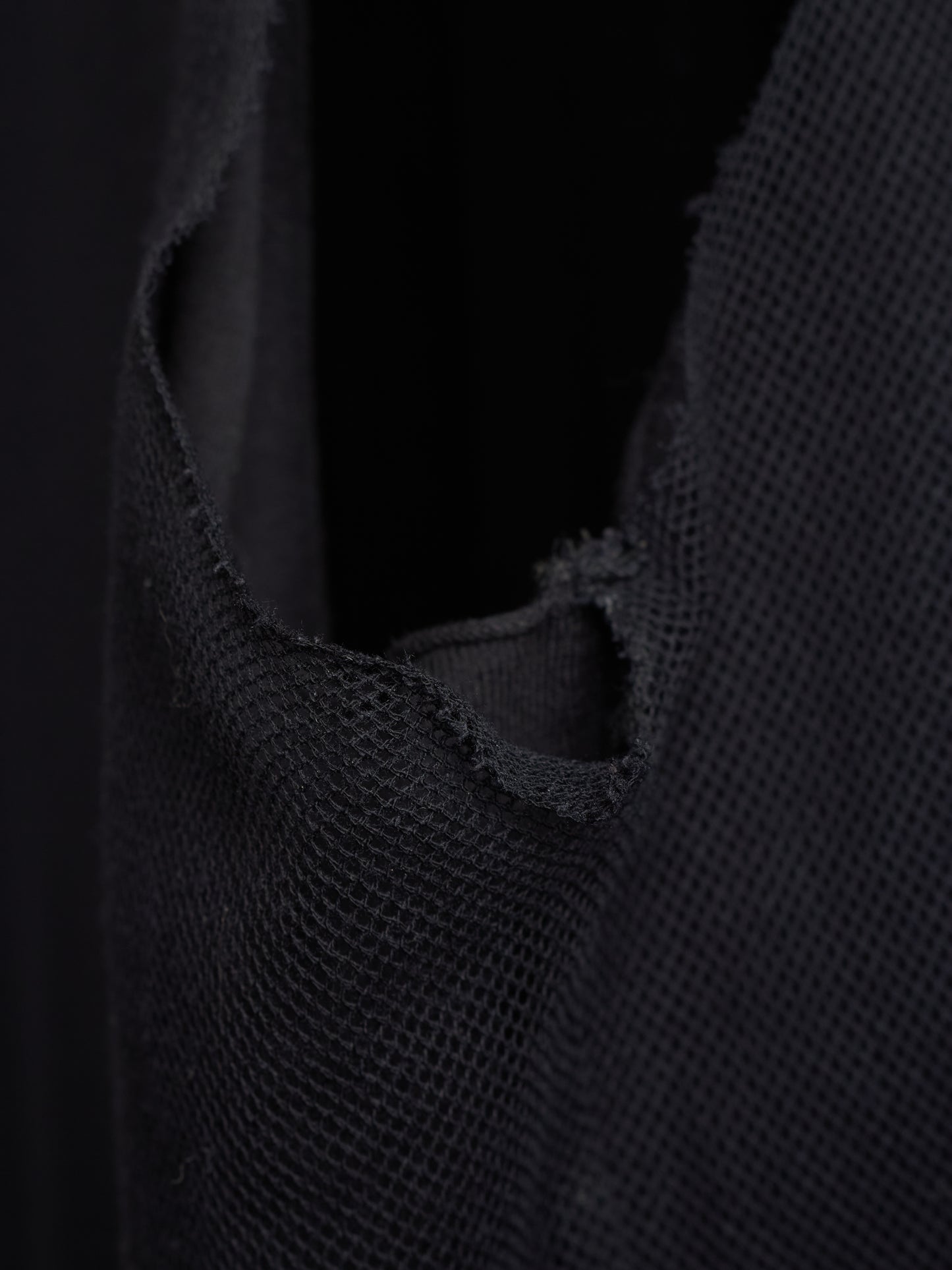 Close-up of a black woven mesh or net fabric with a raw, frayed cut edge against a dark background.