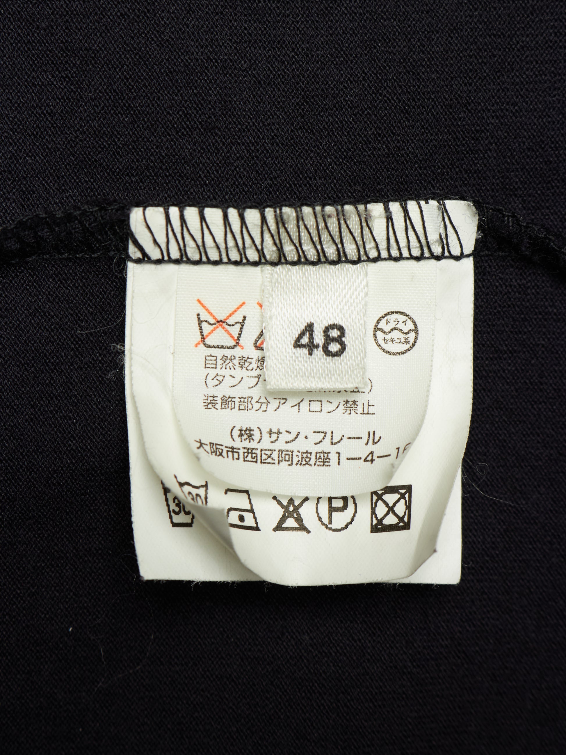 Close-up of a garment's white care label sewn onto black fabric, showing size 48 and Japanese care instructions.