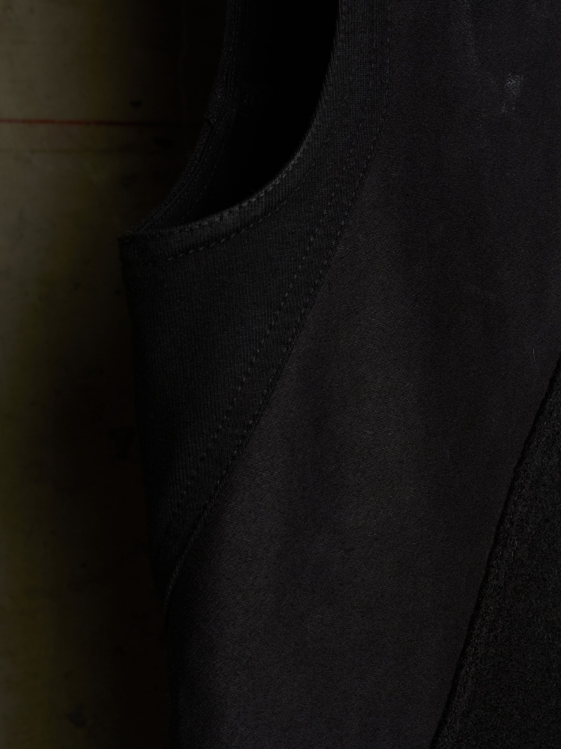 Close-up detail shot of a black sleeveless garment, showing the texture of the fabric and the curved neckline.