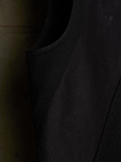 Close-up detail shot of a black sleeveless garment, showing the texture of the fabric and the curved neckline.