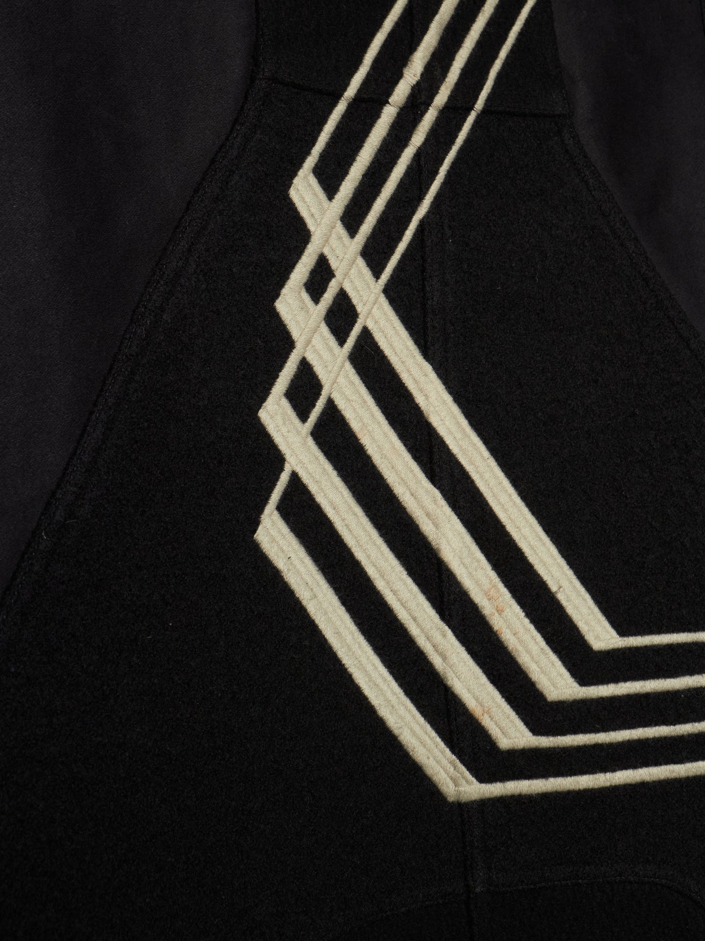 Close-up of a black garment featuring a prominent cream-colored geometric stripe pattern on the side.