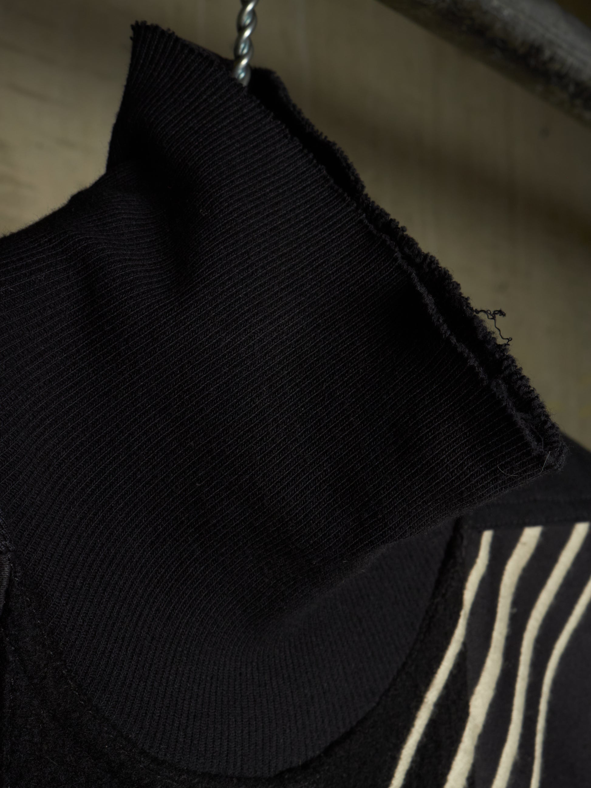 Close-up of a black ribbed knit turtleneck sweater hanging on a metal hanger, showing the raw hem and a striped pattern on the sleeve.