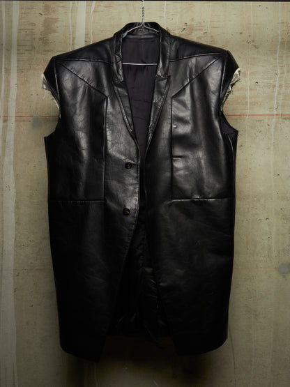 A black leather sleeveless vest hanging against a textured concrete wall, featuring a buttoned front and large front pockets.