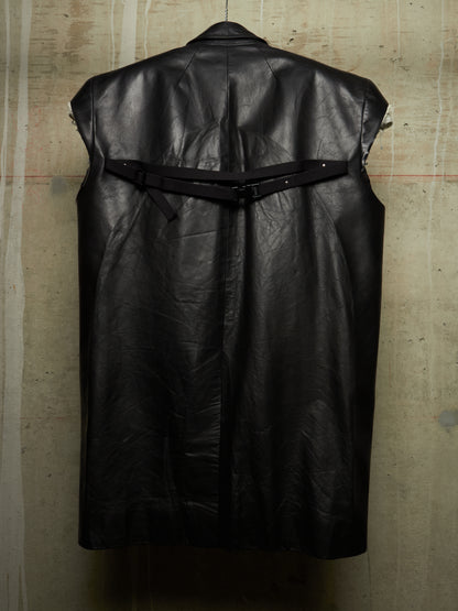 A black leather sleeveless vest with a wide waist belt and buckle closure, shown from the back against a textured concrete wall.