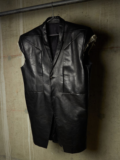 A black leather vest hanging on a hanger against a textured concrete wall.