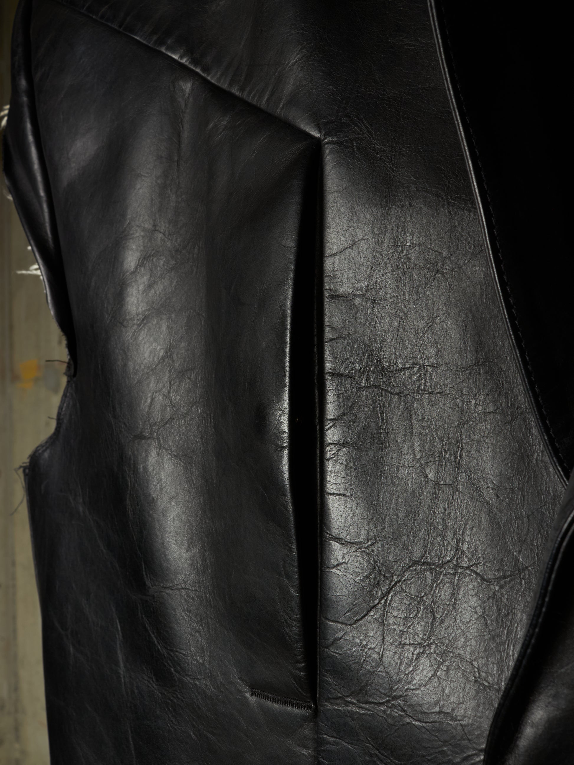Close-up of a black leather jacket showing the textured grain and stitched panel seams.