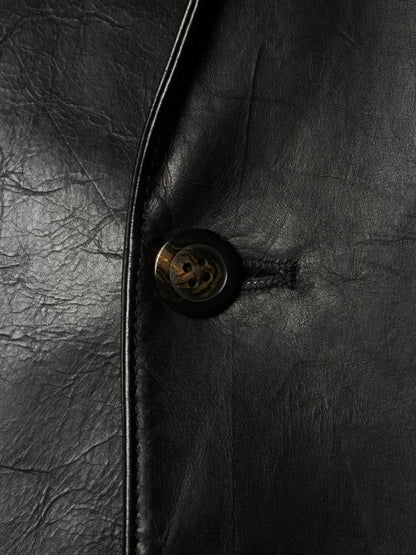 Close-up of a black leather jacket showing the texture of the leather, a black button with a gold-toned center, and a dark metal zipper track.