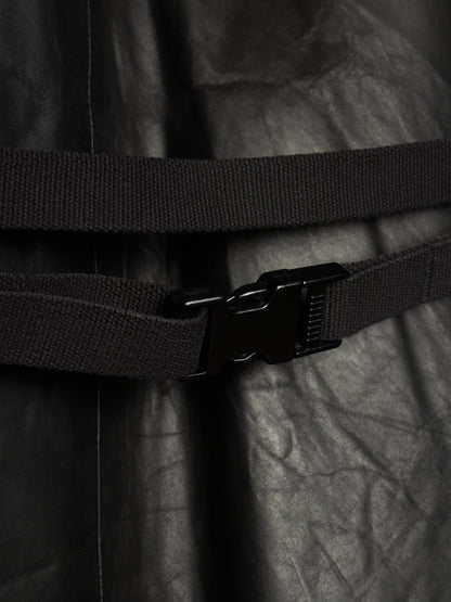 Close-up of a black adjustable web belt with a black plastic quick-release buckle, wrapped around a black crinkled fabric garment.
