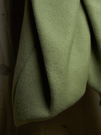 A close-up of draped olive green wool fabric, showing its soft, textured surface and folds.
