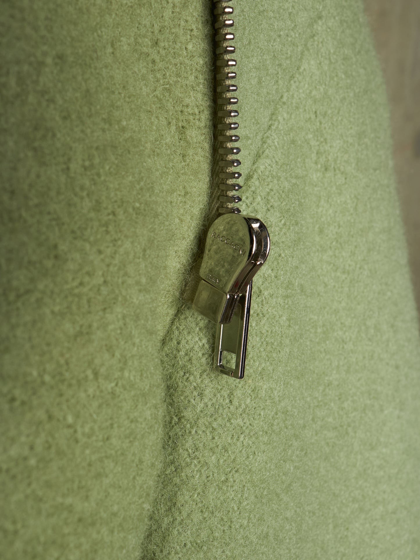 Close-up of a light olive green textured fabric with a silver metal zipper running vertically down the center.