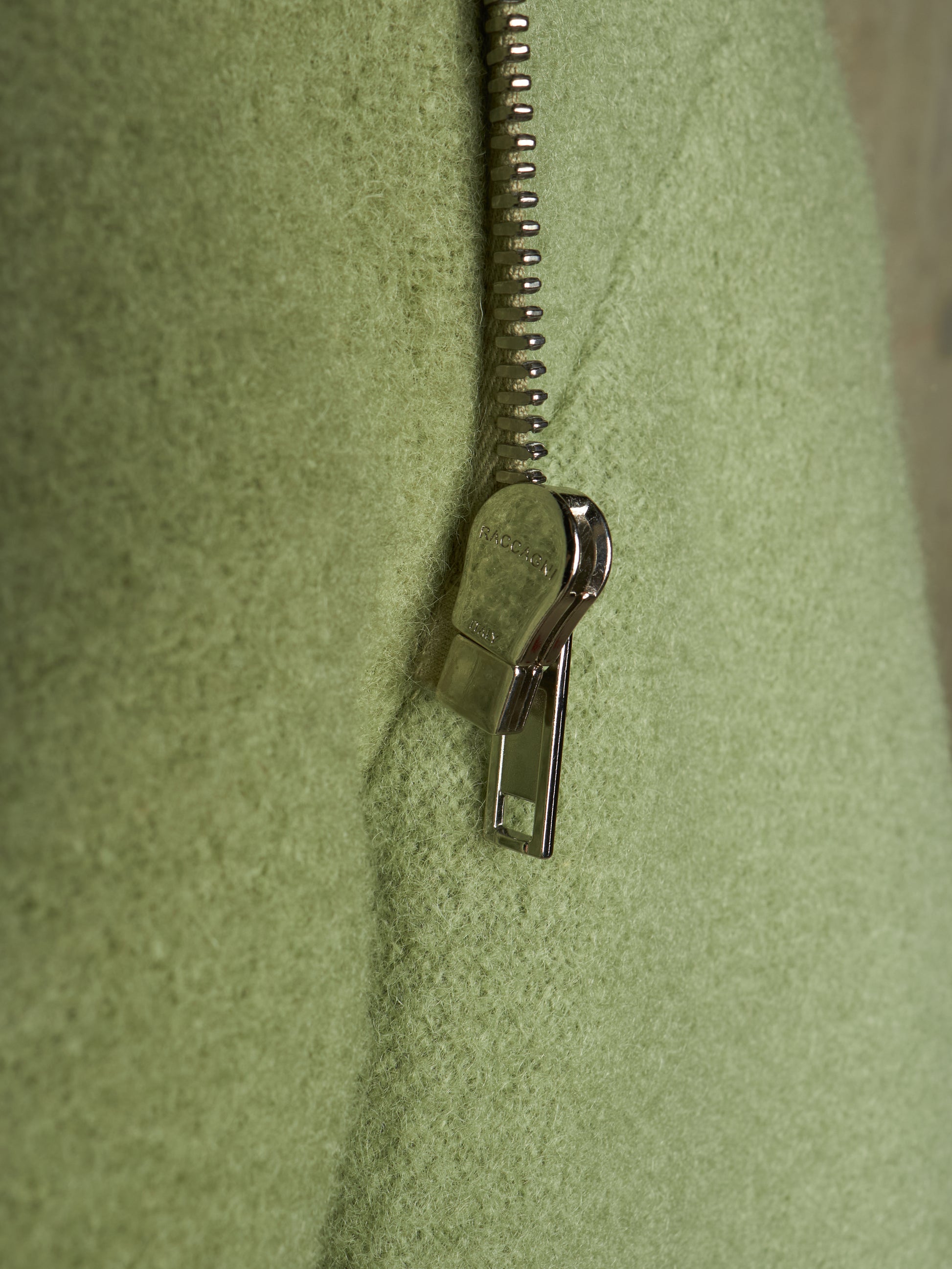 Close-up of a light olive green textured fabric with a silver metal zipper running vertically down the center.