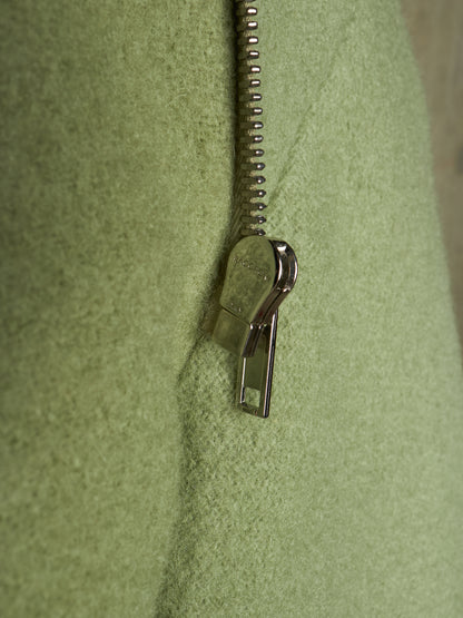 Close-up of a light olive green textured fabric with a silver metal zipper running vertically down the center.