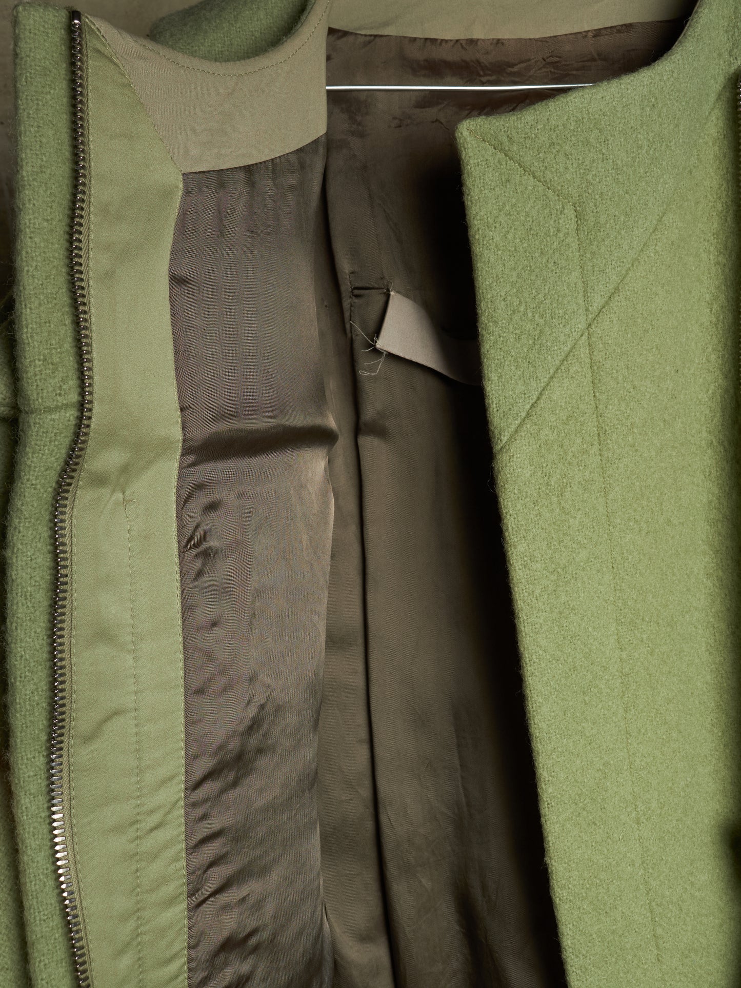 Close-up of an olive green coat with a satin lining, showing the zipper, fabric texture, and interior details.