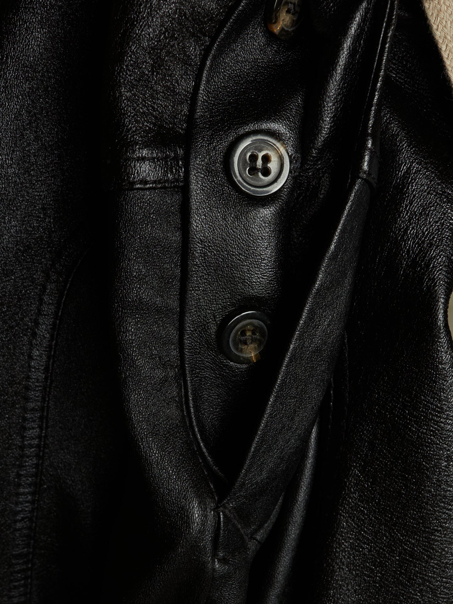 Close-up of a black leather jacket showing the buttoned placket and textured leather fabric.