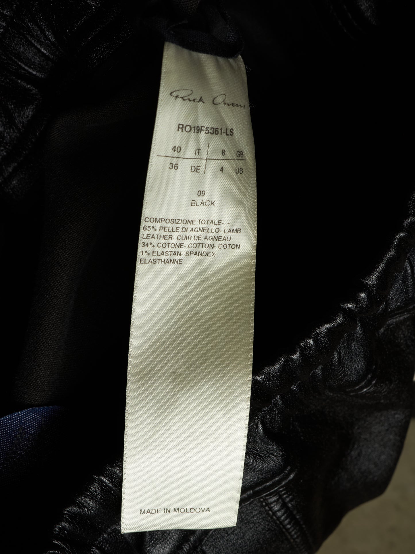 A close-up of a black leather jacket showing a white sewn-in size and material tag with the brand name 'Peck Quinn' visible at the top.