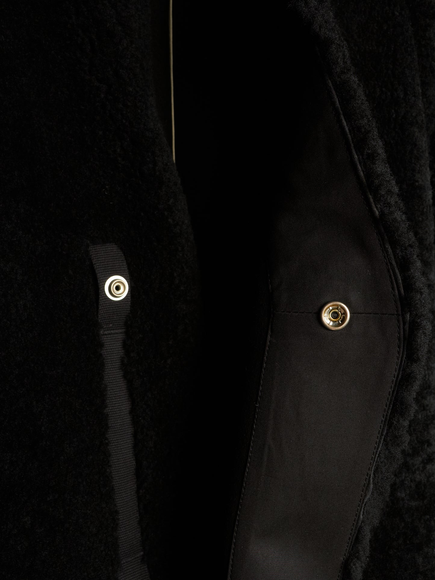 Close-up detail of a black textured coat with a black satin strap and gold-tone snap buttons.