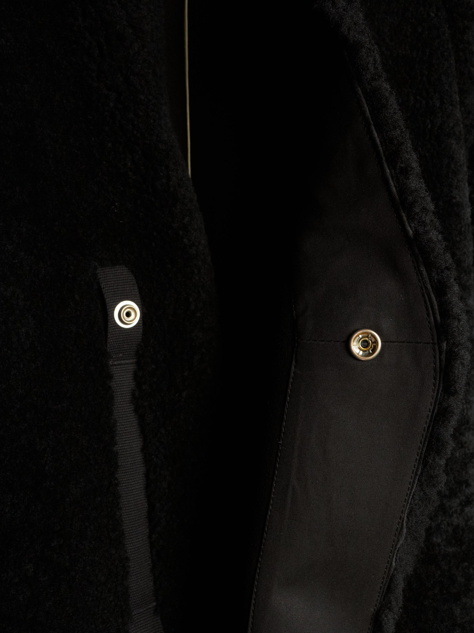 Close-up detail of a black textured coat with a black satin strap and gold-tone snap buttons.