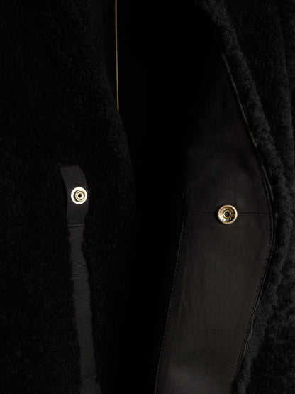 Close-up detail of a black textured coat with a black satin strap and gold-tone snap buttons.