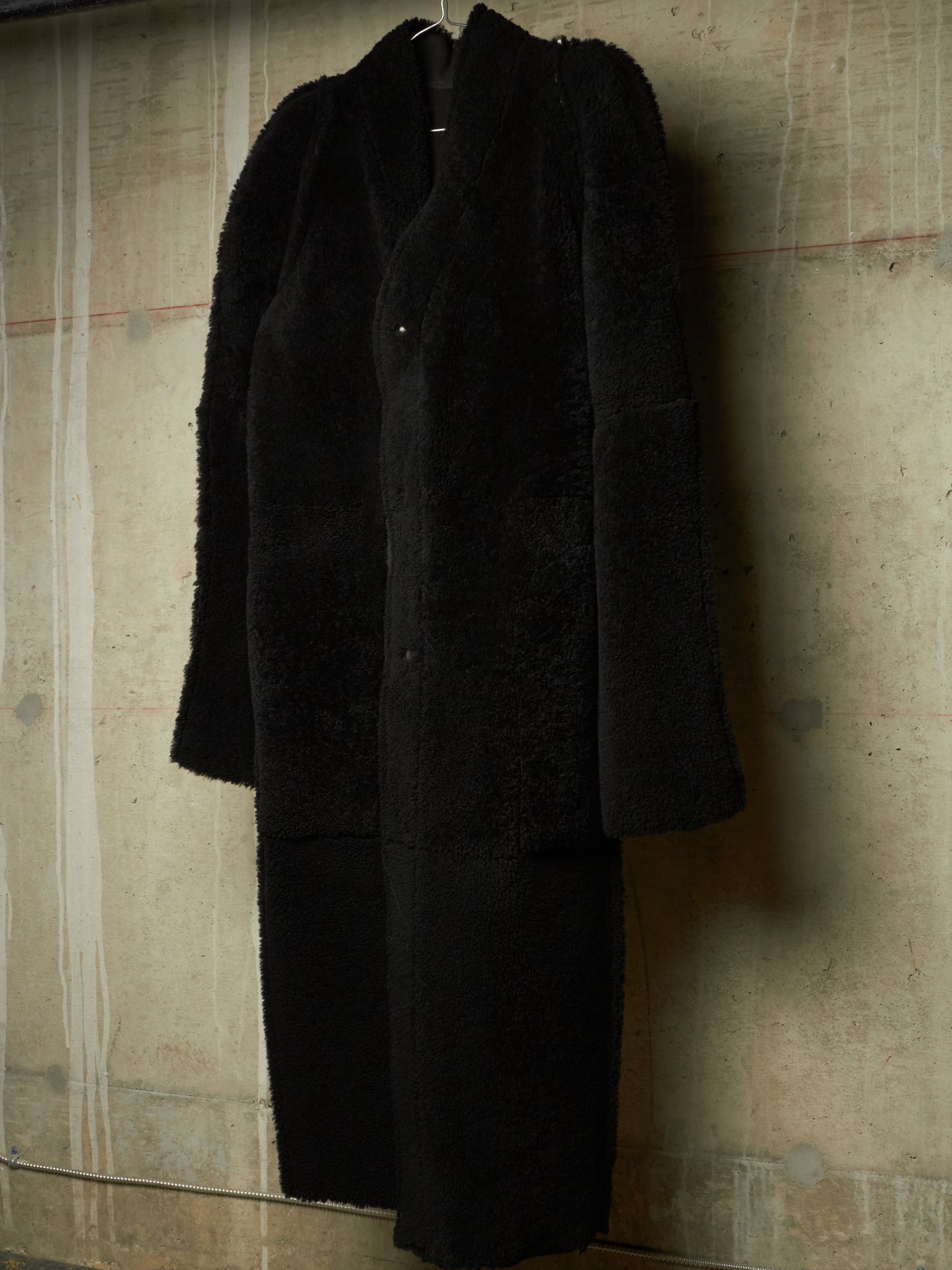 A long black fuzzy coat or dress hanging against a textured concrete wall.