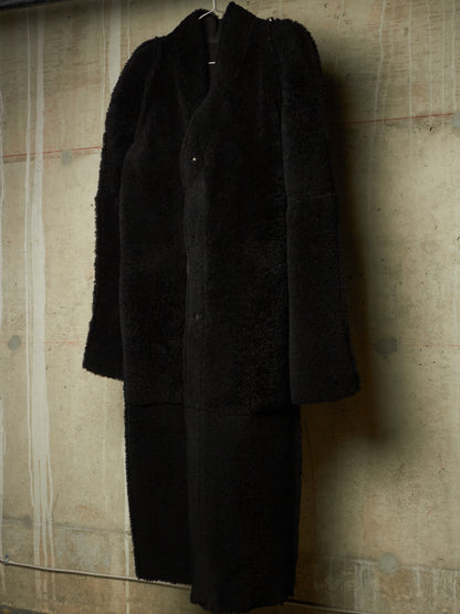 A long black fuzzy coat or dress hanging against a textured concrete wall.