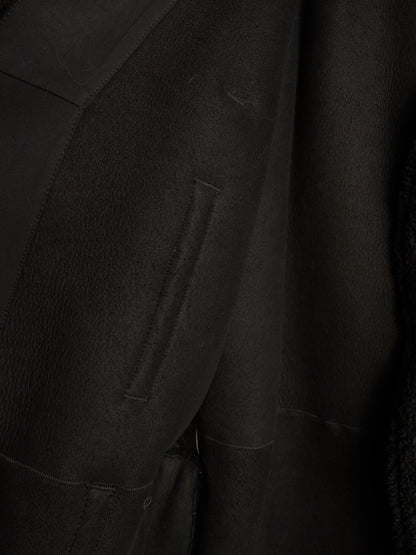 Close-up detail of a black textured jacket or coat showing a vertical welt pocket and fabric texture.