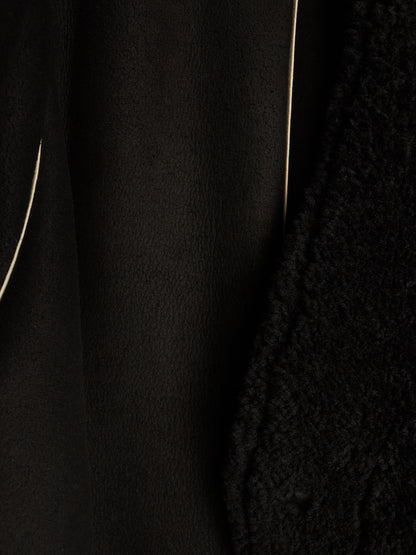 Close-up detail of a black textured garment, showing a smooth matte fabric panel next to a chunky knit or bouclé texture, with thin light-colored piping lines visible.