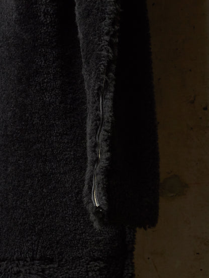 Close-up of a black fuzzy shearling or sherpa jacket with a visible metal zipper running vertically along the edge, set against a dark brown textured background.