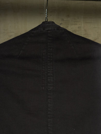Close-up of the back of a black garment hanging on a metal hanger against a textured beige wall.