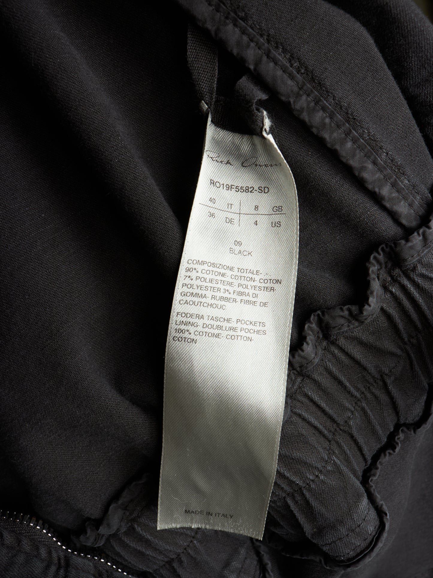 Close-up of a black garment interior showing a sewn-on size and care label that reads Rich Coast and R019F5882-SD.