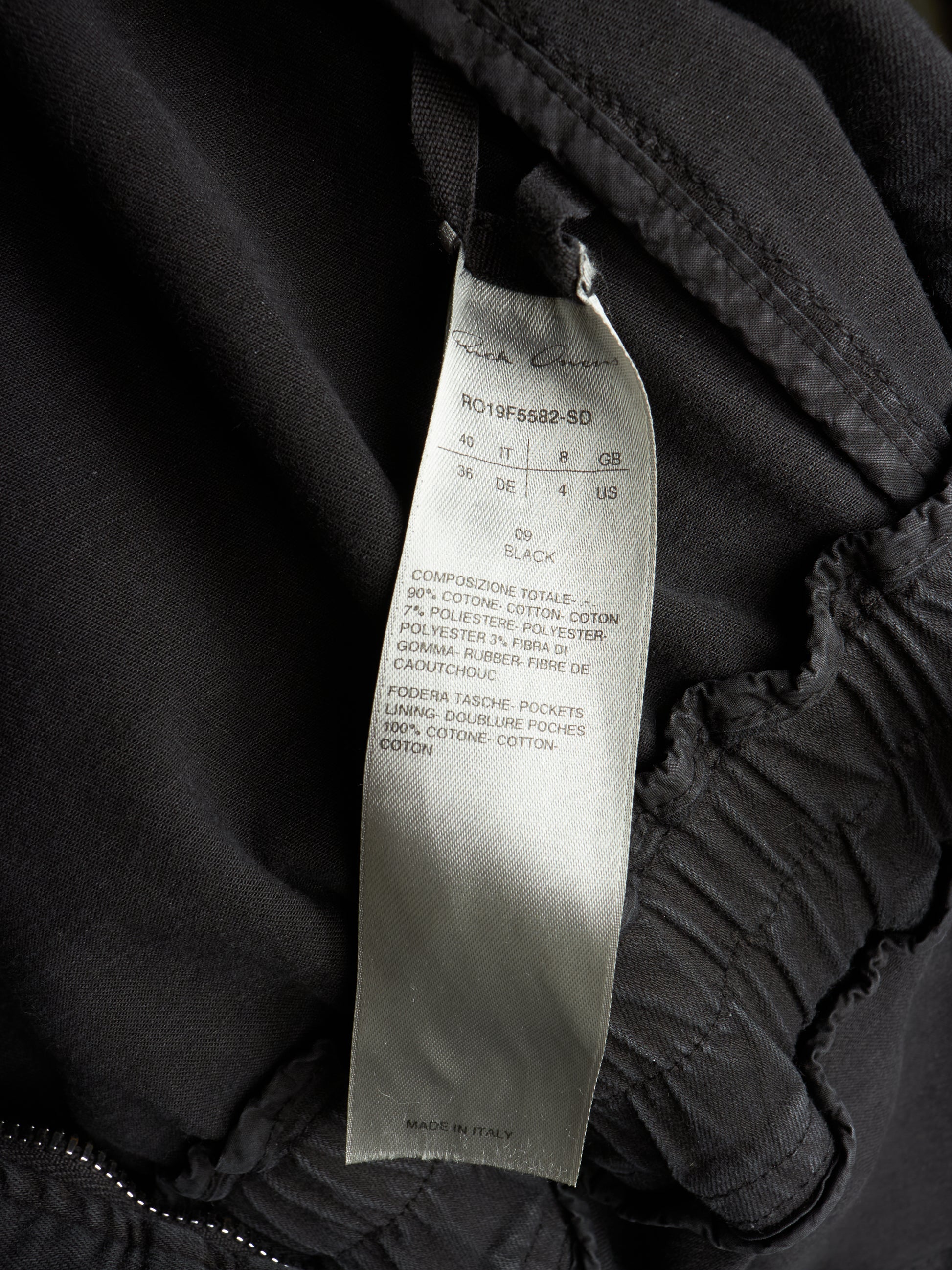 Close-up of a black garment interior showing a sewn-on size and care label that reads Rich Coast and R019F5882-SD.