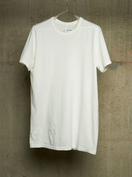 A plain white short-sleeve crewneck t-shirt hanging on a metal hanger against a textured concrete wall.