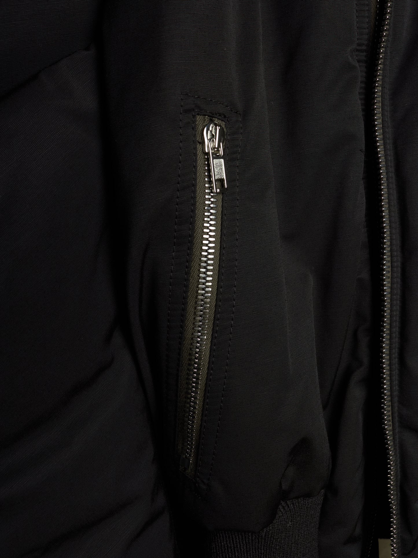 Close-up of a black puffer jacket featuring a vertical zippered pocket with a silver zipper pull and a main front zipper.