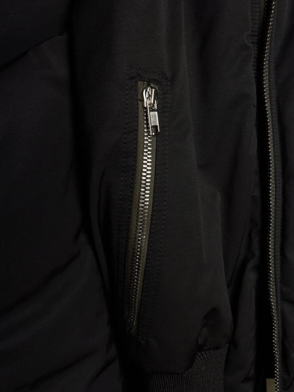 Close-up of a black puffer jacket featuring a vertical zippered pocket with a silver zipper pull and a main front zipper.