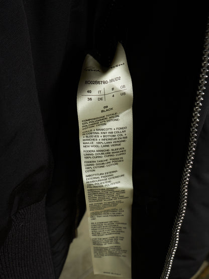 Close-up of a garment interior label attached to a black jacket, with a silver zipper visible on the right side.