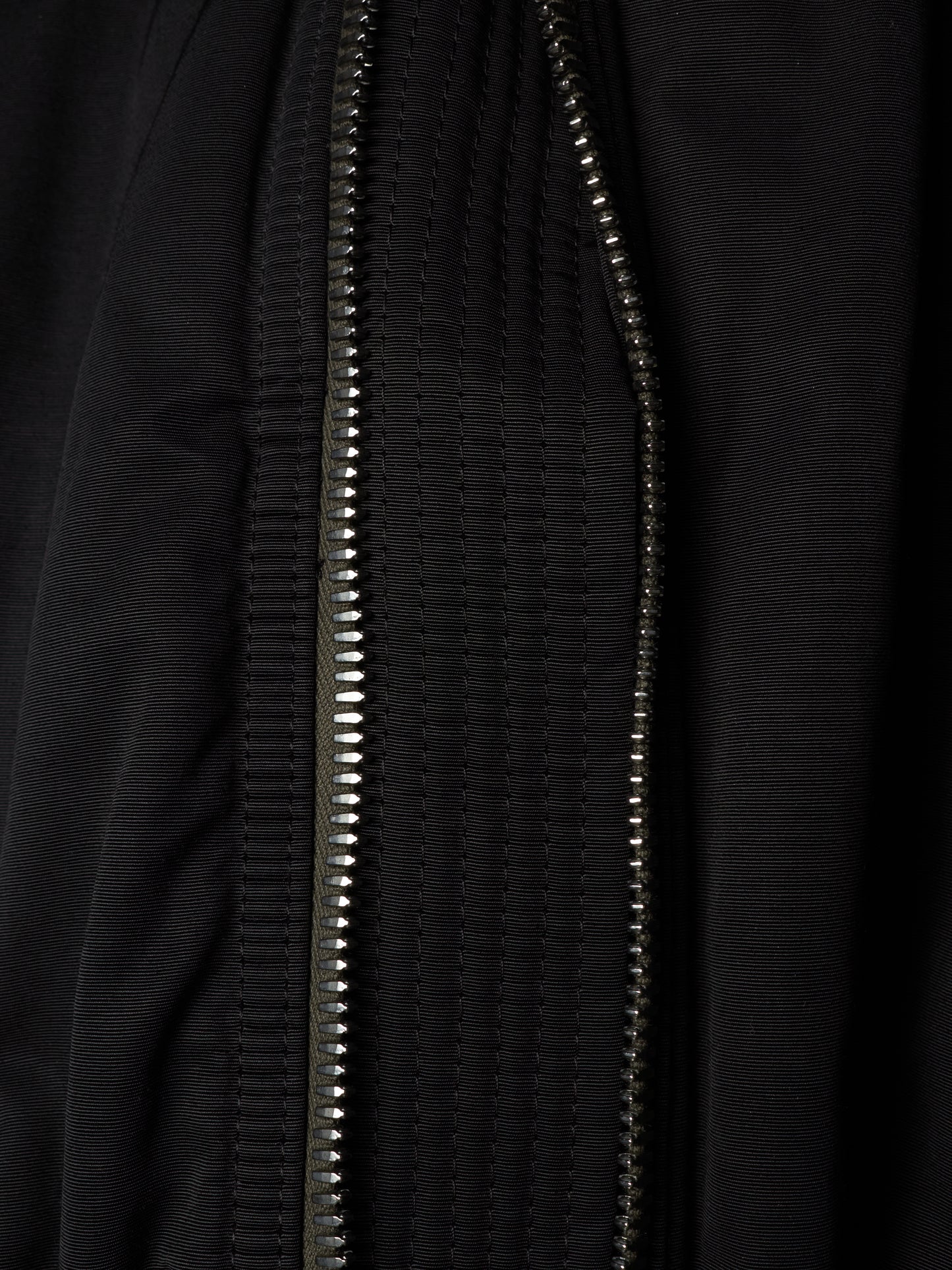 Close-up of a black textured zippered garment, showing the metallic zipper running vertically through the fabric.