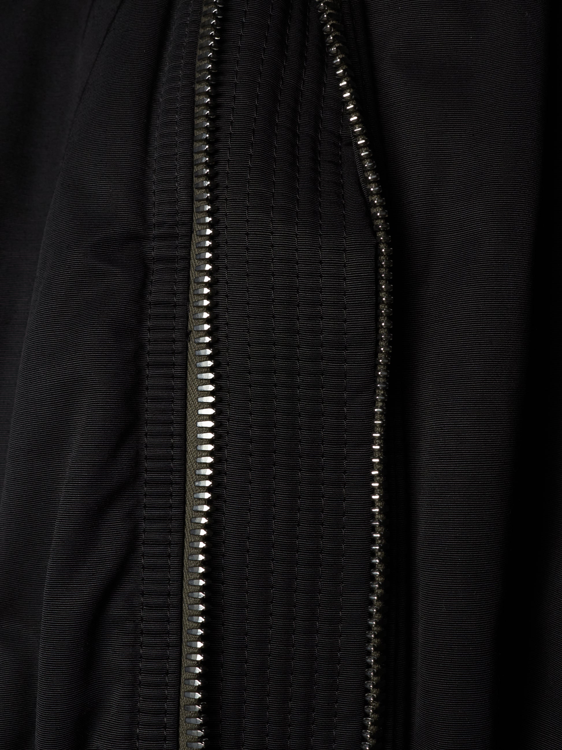 Close-up of a black textured zippered garment, showing the metallic zipper running vertically through the fabric.