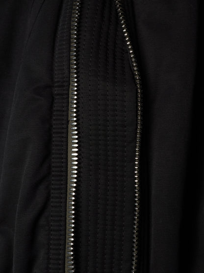 Close-up of a black textured zippered garment, showing the metallic zipper running vertically through the fabric.