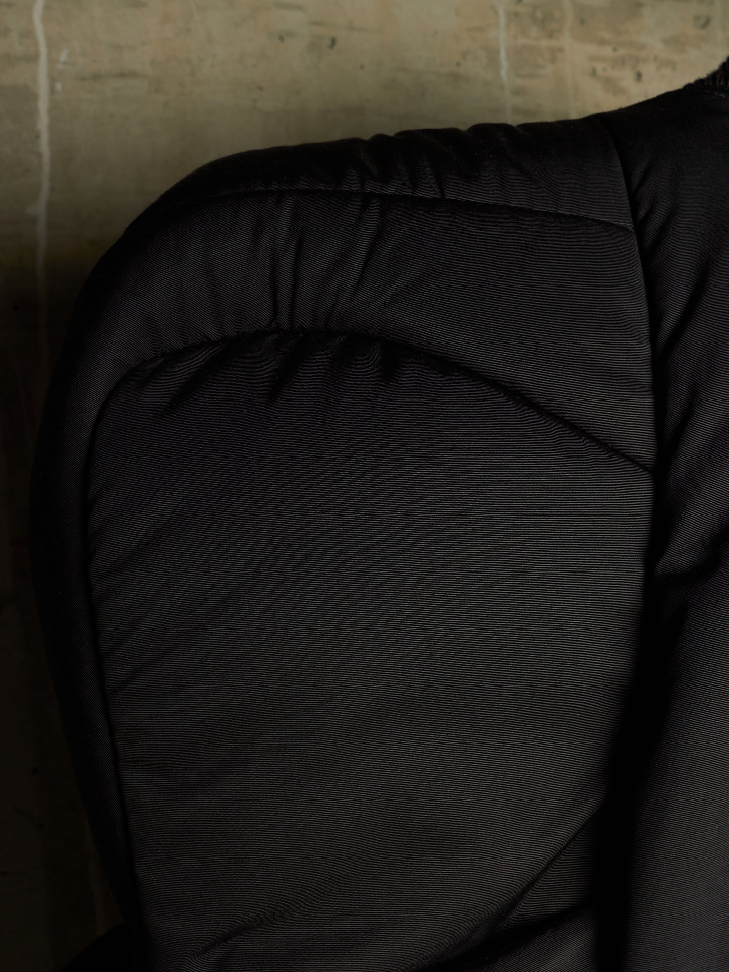 Close-up of a black quilted padded garment, showing the fabric texture and stitching against a dark background.