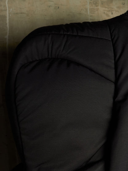 Close-up of a black quilted padded garment, showing the fabric texture and stitching against a dark background.