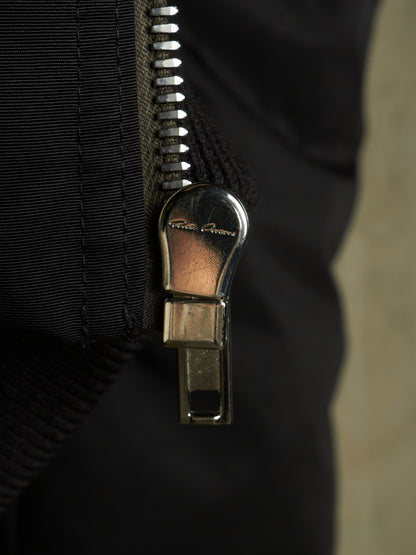 Close-up of a black zippered garment with a shiny silver metal zipper pull featuring the visible brand name 'Kings of NY'.
