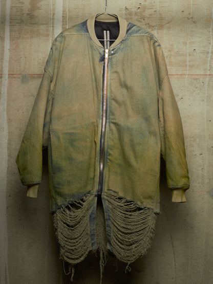 A distressed, oversized zip-up jacket in a faded olive green and tan wash, featuring heavy fraying along the bottom hem and ribbed cuffs, hanging against a textured concrete wall.