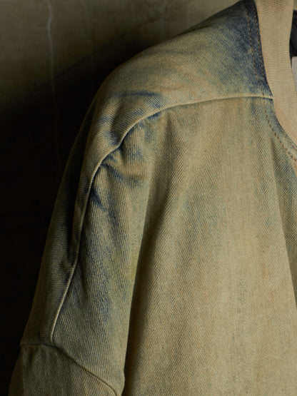 A close-up detail shot of a washed, distressed denim jacket showing the shoulder seam, sleeve, and collar area in a muted beige and blue-gray colorway.