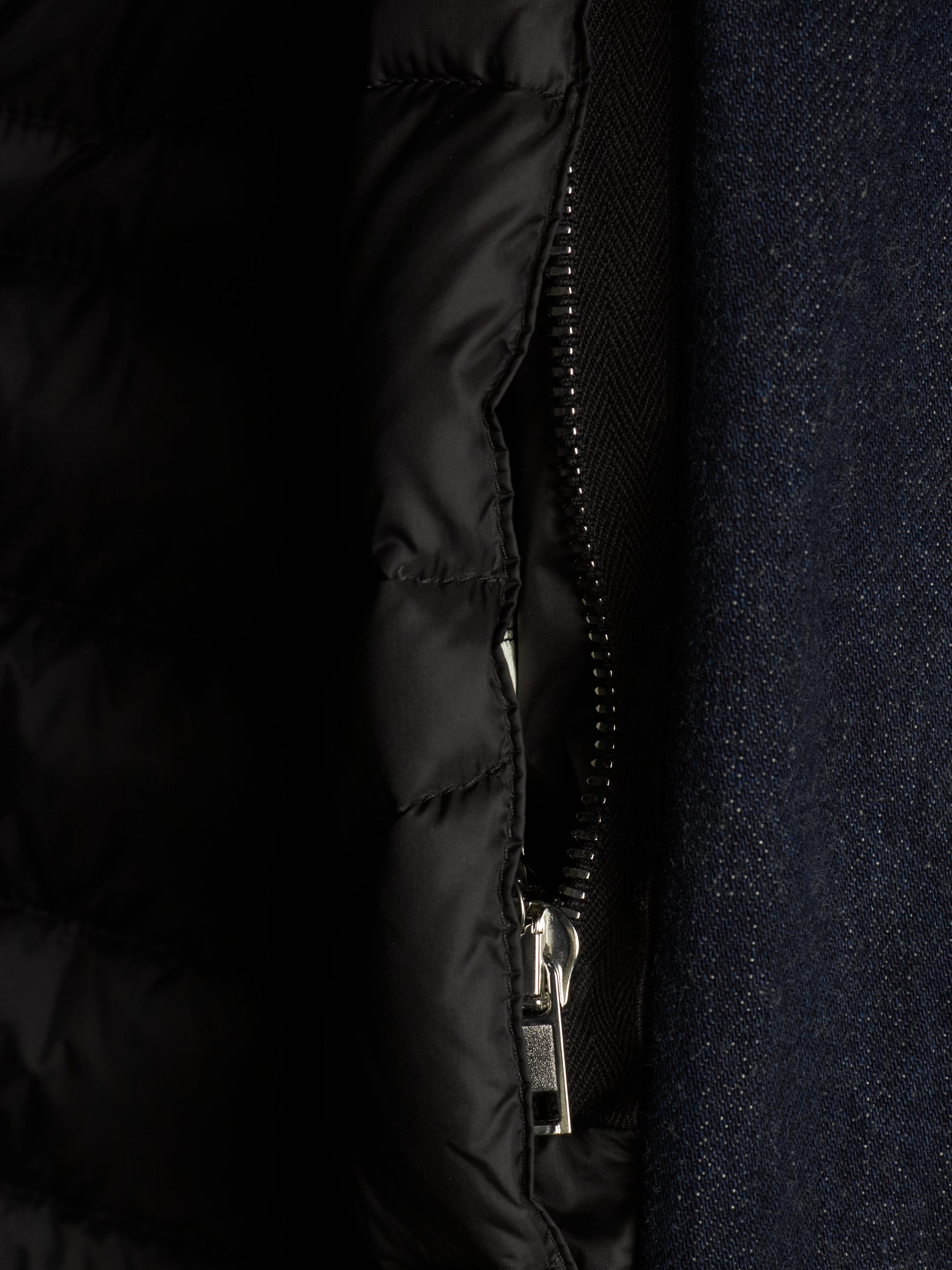 Close-up detail of a black quilted puffer jacket with a silver zipper, shown next to a dark navy textured fabric.