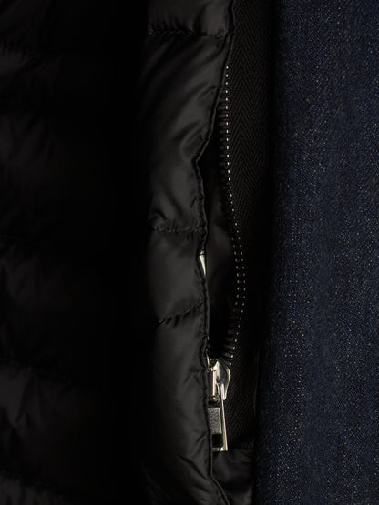 Close-up detail of a black quilted puffer jacket with a silver zipper, shown next to a dark navy textured fabric.