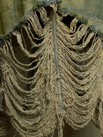 Close-up of a heavily distressed garment or textile with extensive frayed, tattered edges in beige and tan, showing dense loose threads and worn fabric layers.