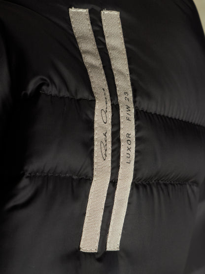 Close-up of a black puffer jacket featuring two vertical light gray ribbed fabric stripes with embroidered branding and script.