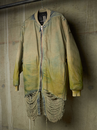 A distressed, oversized zip-up jacket with a yellow-green and blue-gray acid-wash finish, featuring a raw, frayed hem and ribbed cuffs, hanging against a textured concrete wall.