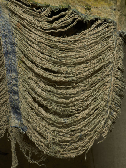 A close-up of a heavily distressed denim garment, showing frayed, shredded layers of light blue and beige denim fabric.