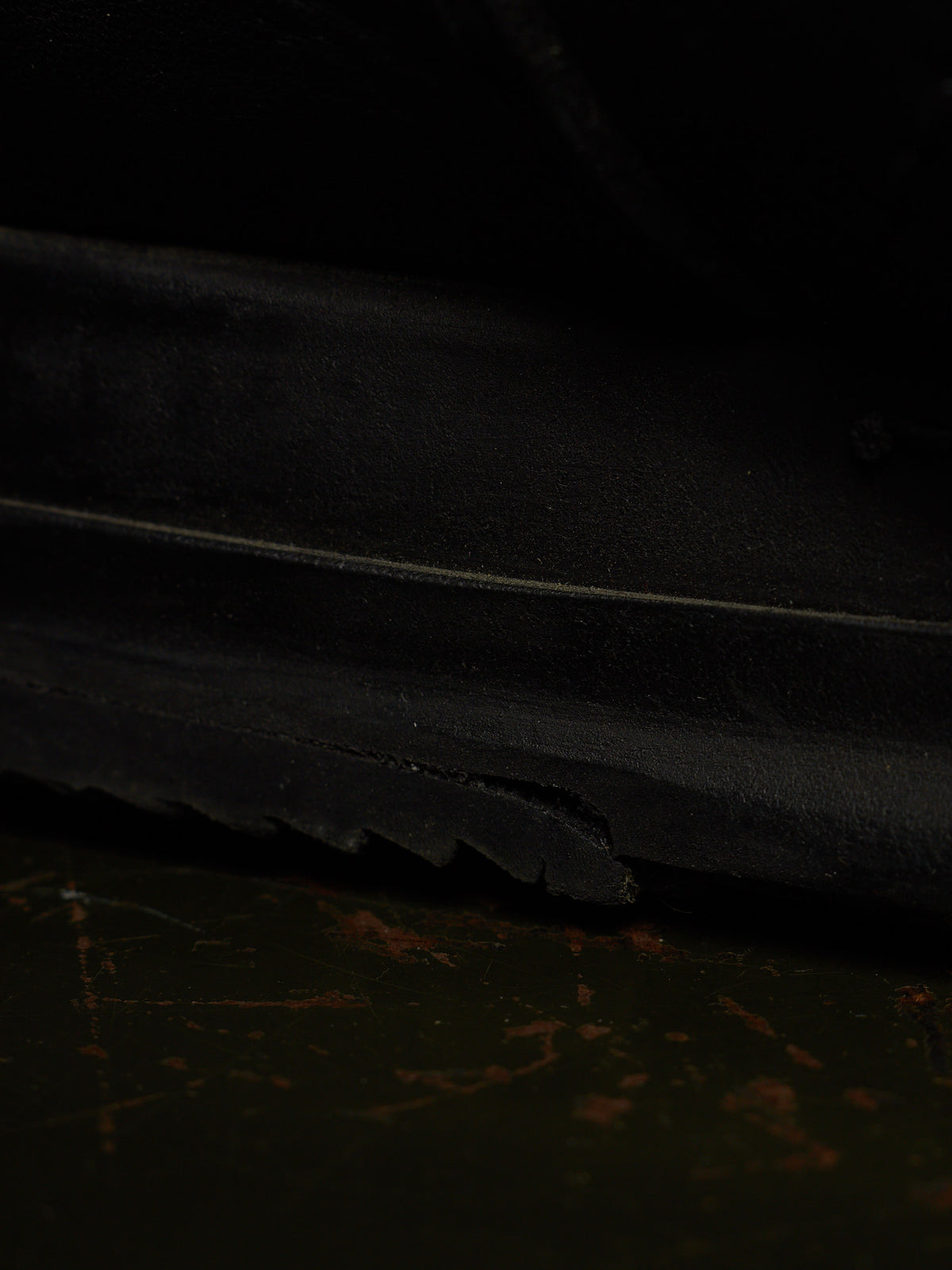 Close-up of a black rubber sole with a visible crack along the edge, resting on a dark, worn surface.
